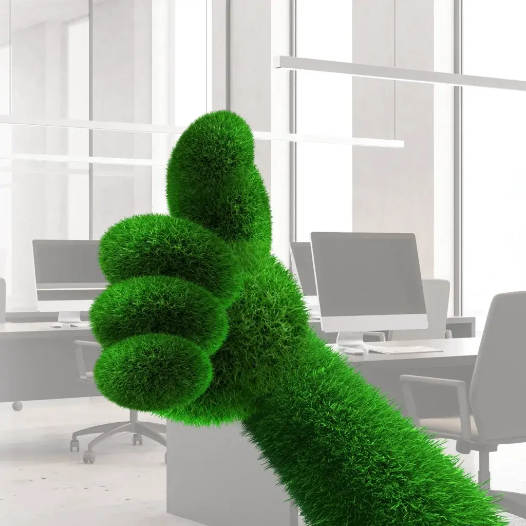 A large, green, grass-like hand gives a thumbs up gesture, set against a modern office background with computers and large windows.